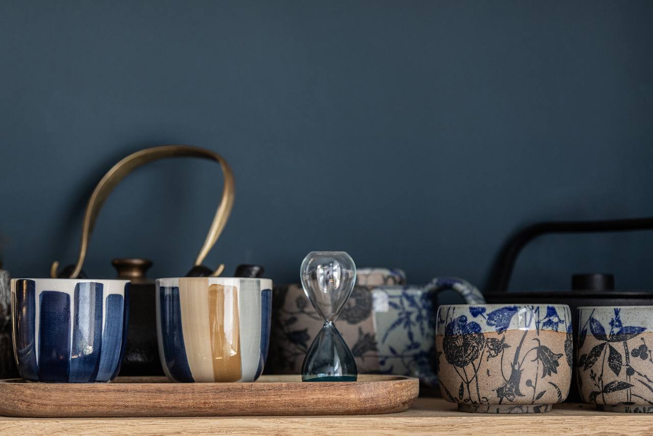 Holzregal mit Keramiktassen vor blauer Wandfarbe 