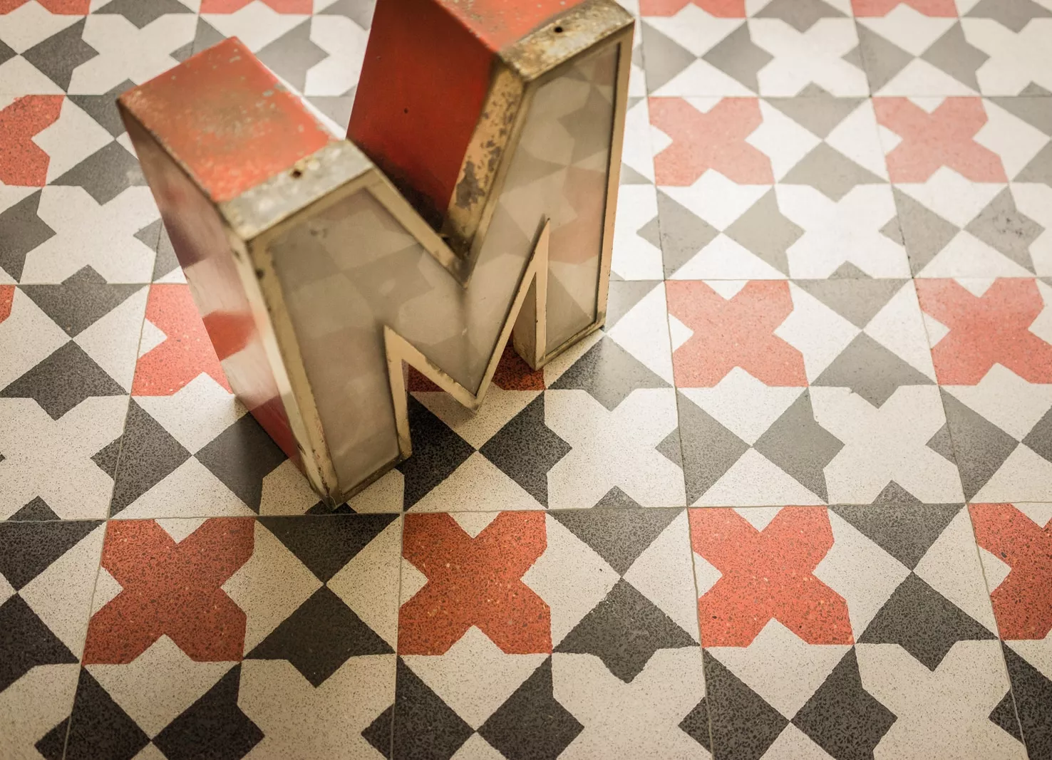 gemusterte Terrazzoplatten mit schwarz/rot/weißen Elementen und einem großen M darauf